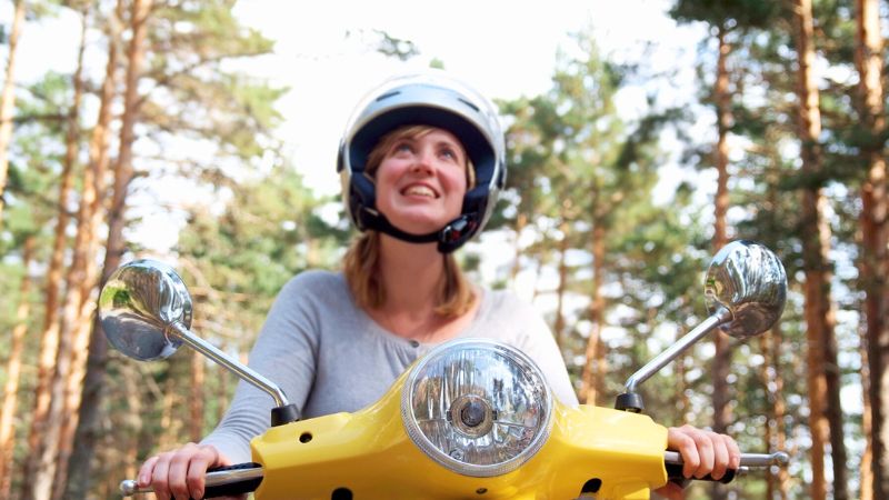 Smiling woman riding a yellow Vespa through a forest in Montreal