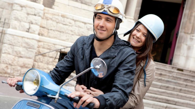 Smiling couple riding a blue Vespa through the historic streets of Montreal.