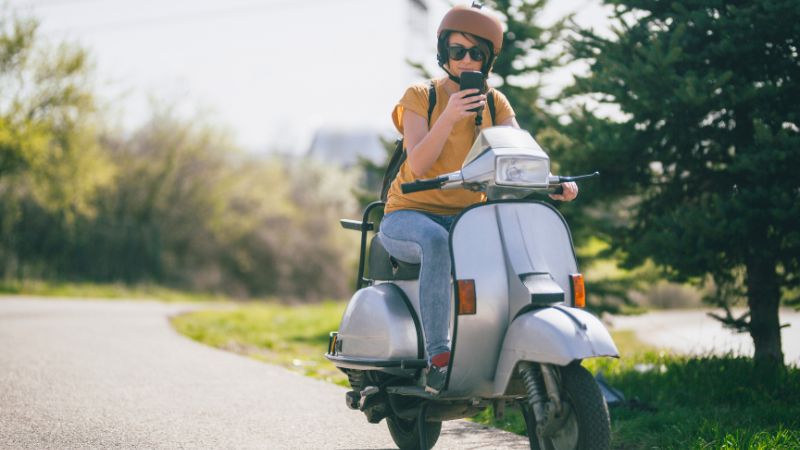 Woman riding a vintage Vespa safely through a scenic park in Montreal.